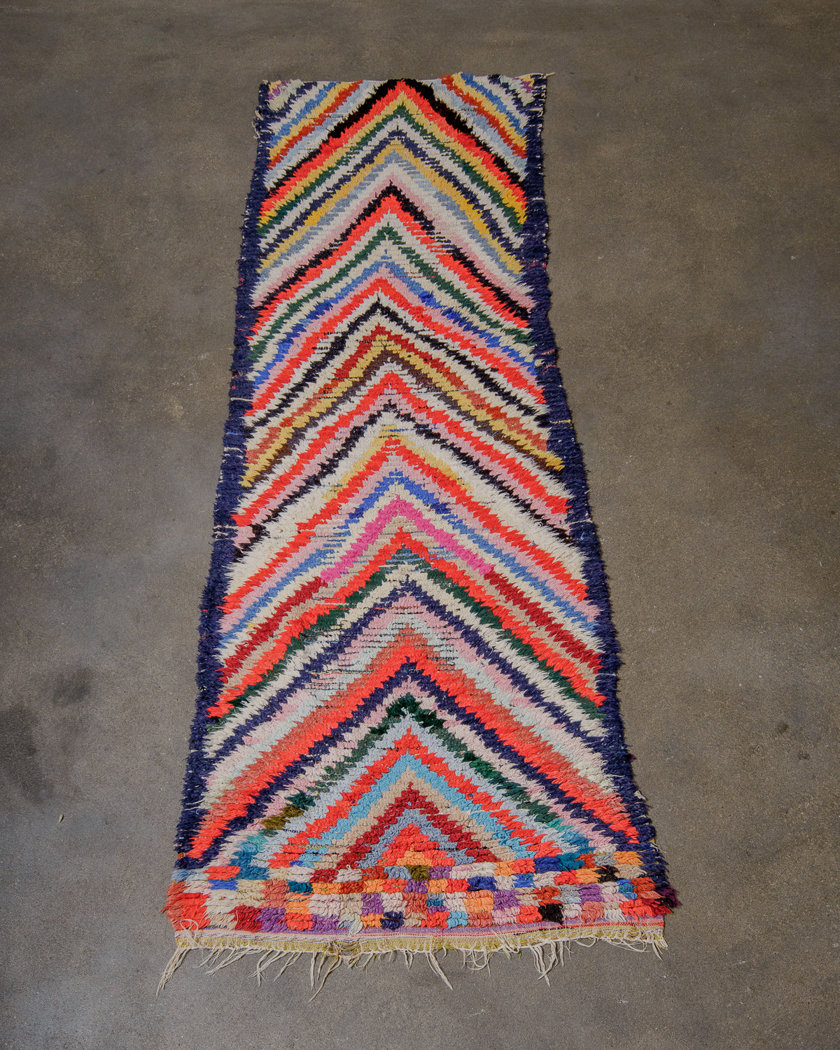 Colourful herringbone patterned rug against cement floor.